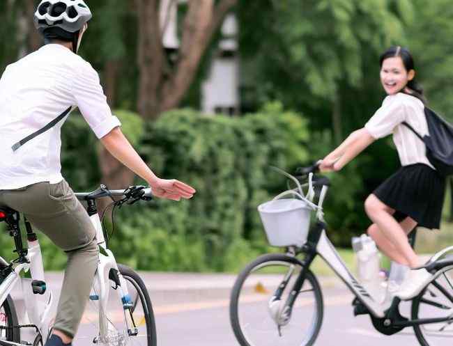 A man cycling regular bicycle looks anxious chasing a lady cycling e-bike.