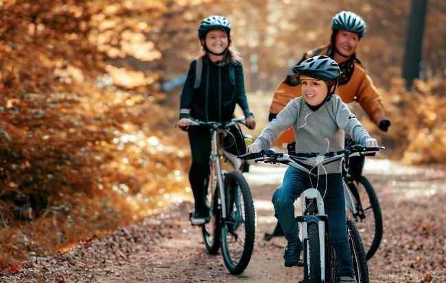 Family cycling tour in the wood during the autumn session. Electric bikes not only give joyfulness but also a healthy family life.